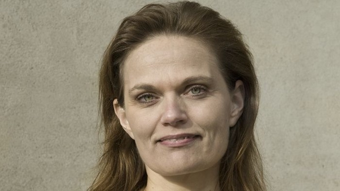 En kvinde med langt, mørkt hår og blå øjne smiler til kameraet.