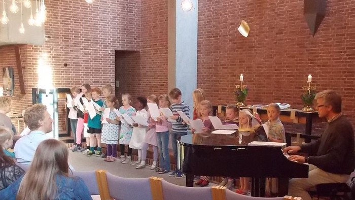 En gruppe børn synger i en kirke, mens en mand spiller piano