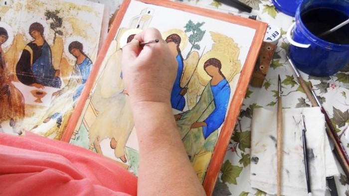 En hånd maler en religiøs scene på papir med blå farge