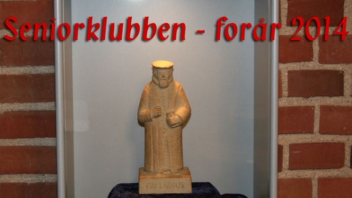 En lille statue af en munk med kapusjin foran rød mursten og tekst