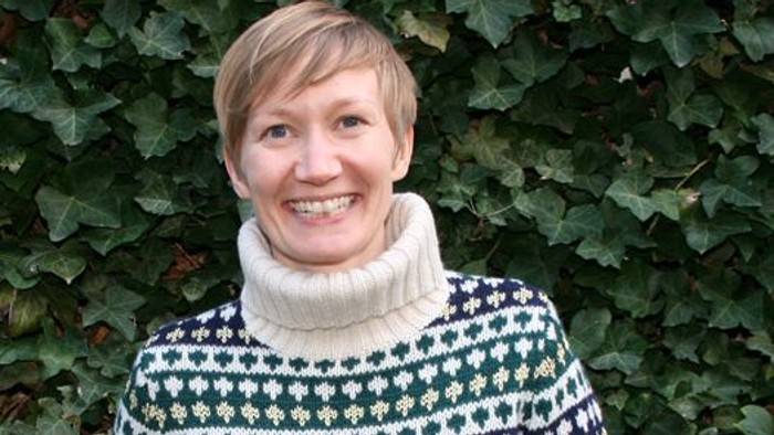 Kvinde med kort hår og mønstret pullover står foran grønne klatreplanter
