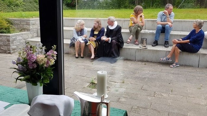 En gruppe mennesker sidder på benker og taler sammen i en træløs park.
