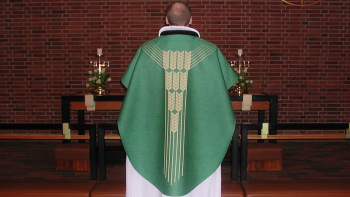 En præst i grøn liturgisk kappe står ved alteret