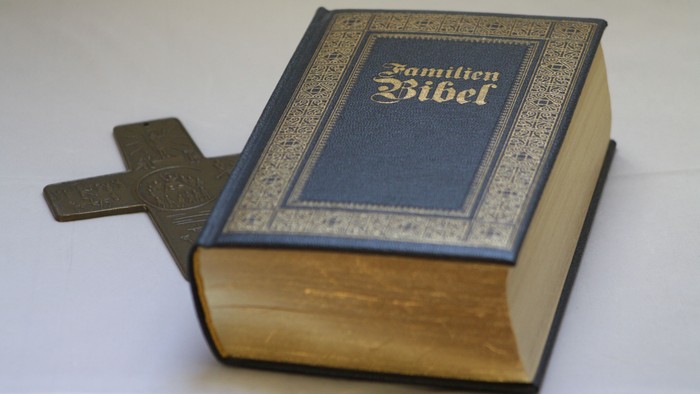 Ein aufgeschlagenes Buch mit dem Titel "Familien Bibel" und einem Kreuz als Lesezeichen.