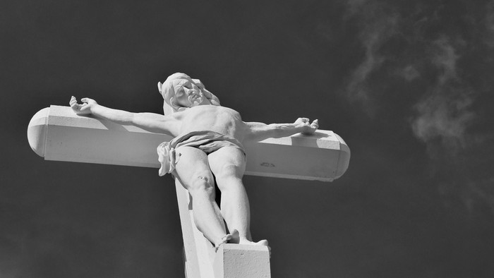 Die Statue eines Mannes an einem Kreuz vor dunklem Himmel.
