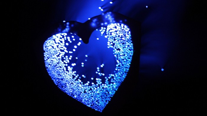 Ein beleuchtetes Herz schwebt im dunklen Raum, umgeben von funkelnden Lichtern.