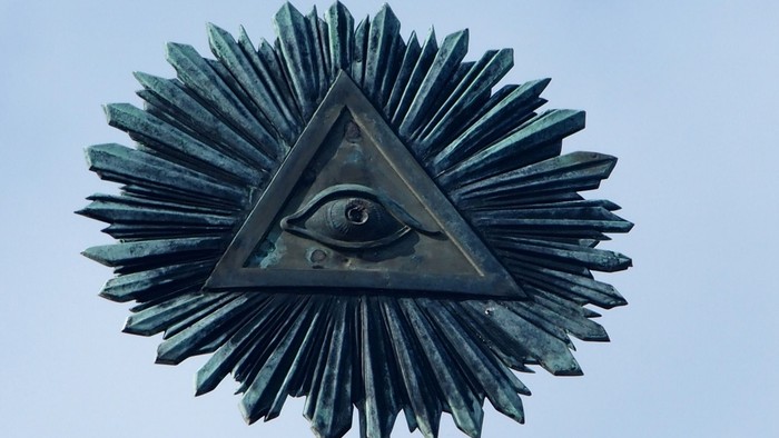 Das Bild zeigt eine Bronzestatue mit einem dreieckigen Auge in der Mitte.