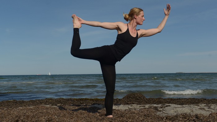 En kvinde udfører yoga på en klippe ved stranden.