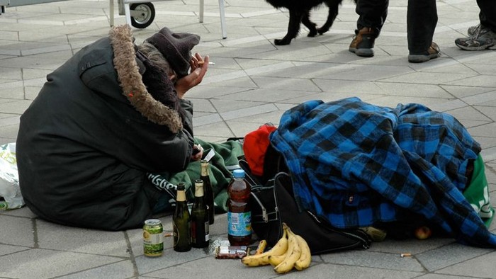 En person sitter på gaden med en flaske og en banan ved siden af sig