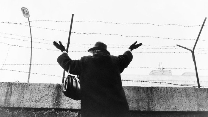 En person med udstrakt arme ved en barberet mur og barbed wire.