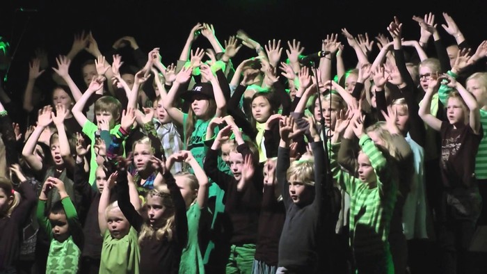 En gruppe børn i grønne t-shirts danser og har armeene i luften