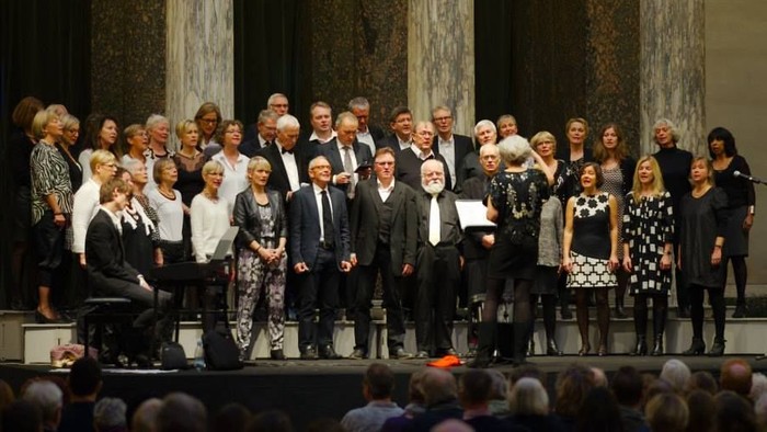 En stor gruppe af formelt klædte personer står sammen på en scene.