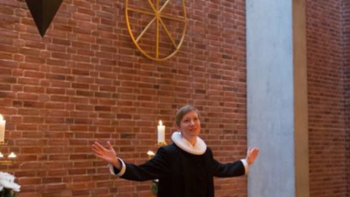 En præst står ved alteret i en kirke og holder to hånders oppe.