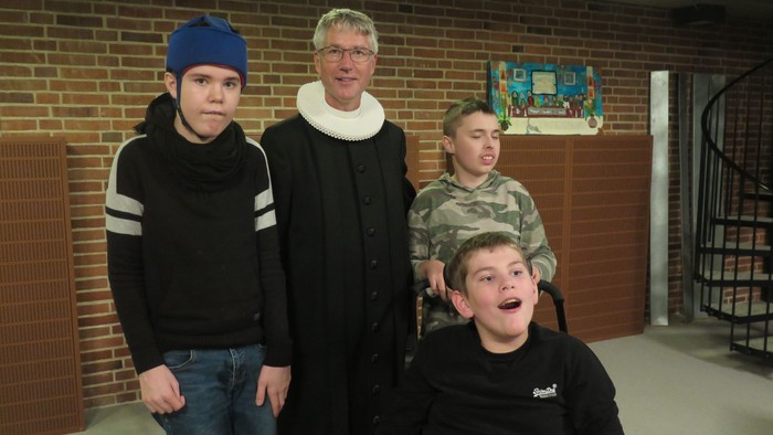 Fire mænd står sammen i et rum med mur af røde mursten. En af mændene sidder i en hjuletstol.