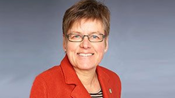 Eine Frau mit kurzem Haar und Brille trägt eine rote Jacke und lächelt.