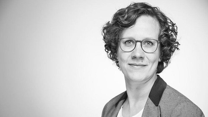 Frau mit Brille und Jacket posiert für ein Schwarz-Weiß-Foto.