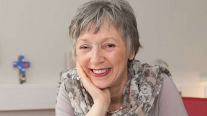 Eine Frau mit grauen Haaren und einem Schal lächelt in die Kamera.