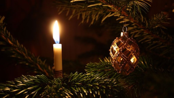 En lysende lykt mellem grønne grenar og et glasornament.