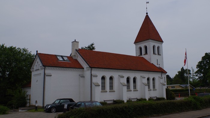 En hvid kirke med rødt tag og tårn med flag i forgrunden