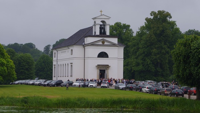 En hvid kirke med tårn og klokke ved en sø i grønne omgivelser
