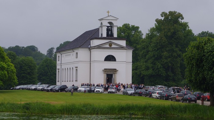 En hvid kirke med tårn og klokke ved en sø i grønne omgivelser