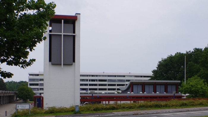 En moderne kirke med høj tårn ved en vejskrydsel.