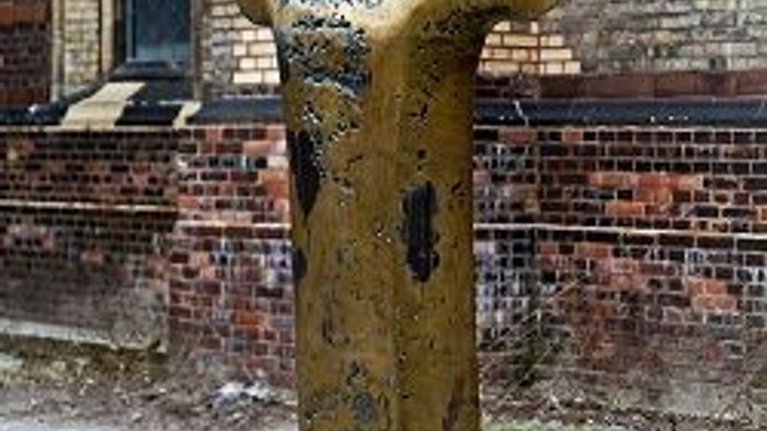 Goldener Torso auf Sockel vor Backsteingebäude