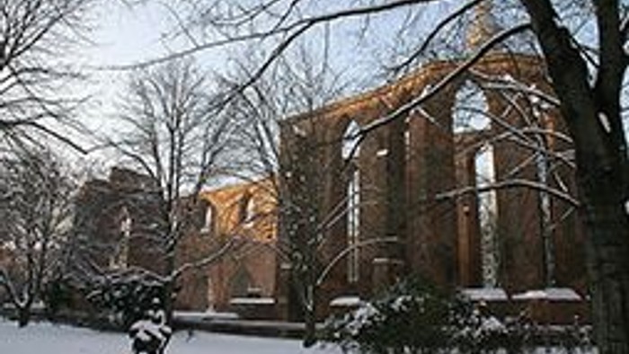 Ein schneebedeckter Park mit einem großen Backsteingebäude im Hintergrund.