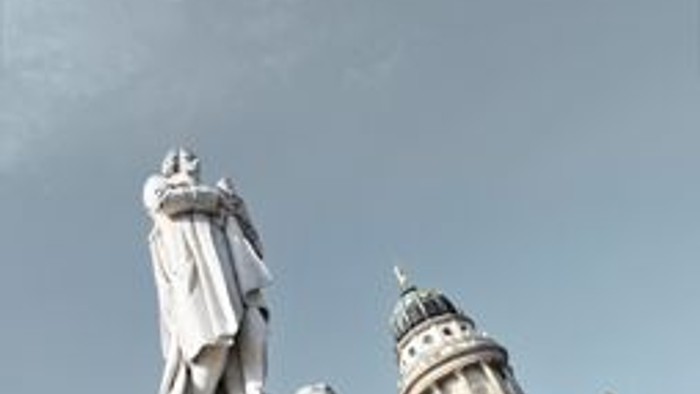 Das Bild zeigt eine Statue vor einem Gebäude mit Uhrturm.