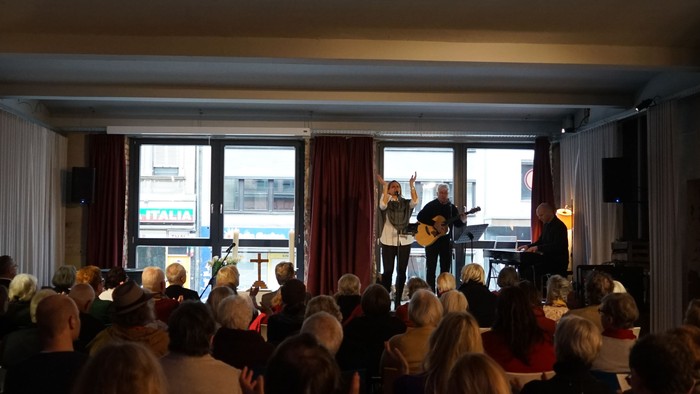 Eine Gruppe von Menschen schaut einem Vortrag auf einer Bühne zu.