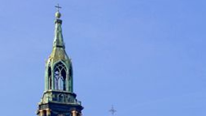 Ein Kirchengebäude mit hohem Turm und grünem Dach vor blauem Himmel