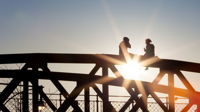 Zwei Personen sitzen auf einer Metallbrücke bei Sonnenuntergang