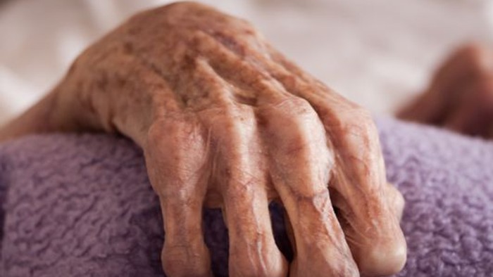 Alte, knochige Hand ruht auf einem lila Kissen