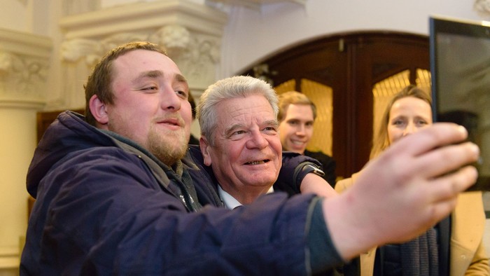 Zwei Männer machen ein Selfie, im Hintergrund sind weitere Personen.