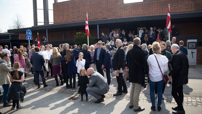 En gruppe af mennesker står foran et murstensbygning med flag.