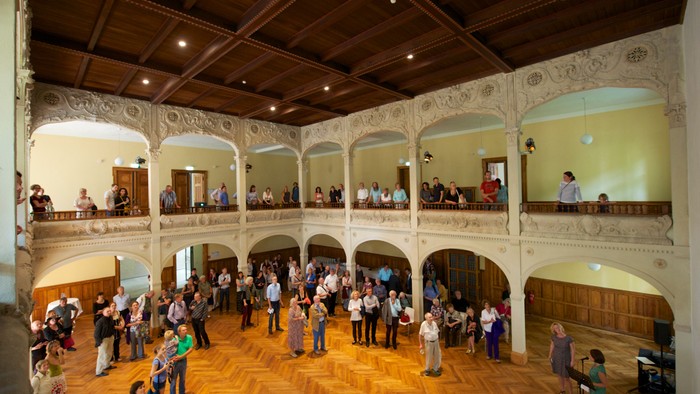 Großer Saal mit vielen Menschen, Holzfußboden, hohe Decke, Balkone