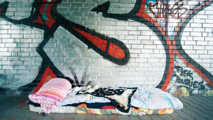 Ein Obdachloser schläft auf einer Decke vor einem Graffiti-Wand.