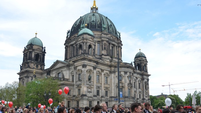 Große Menschenmenge vor prächtigem Dom mit Kuppel und Türmen, viele halten rote Luftballons