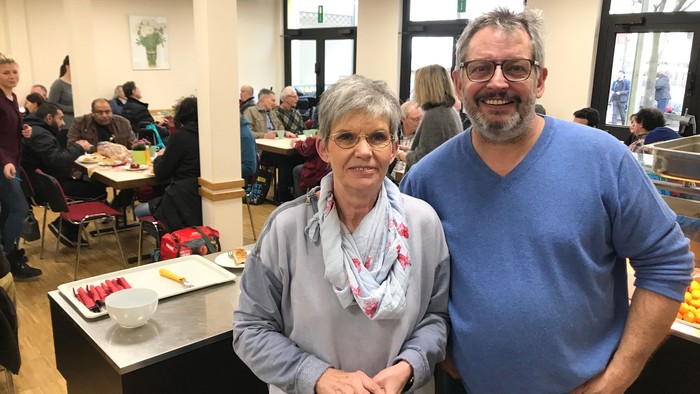 Ein Paar steht in einem Raum mit anderen Menschen an Tischen.