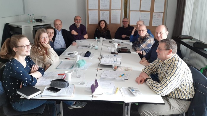 Ein Team trifft sich in einem Besprechungsraum und diskutiert um einen Tisch voller Papiere.