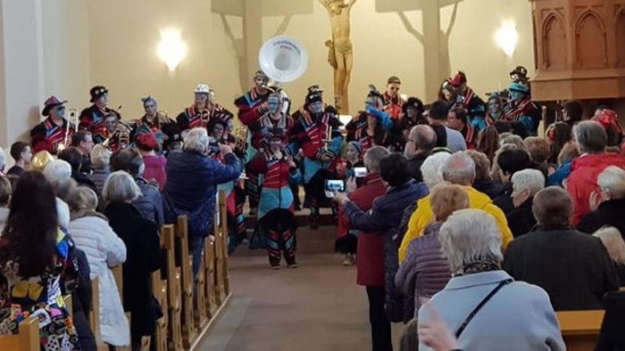 Eine große Gruppe von Menschen versammelt sich in einer Kirche, einige stehen, andere sitzen, und ein Chor singt vorne.