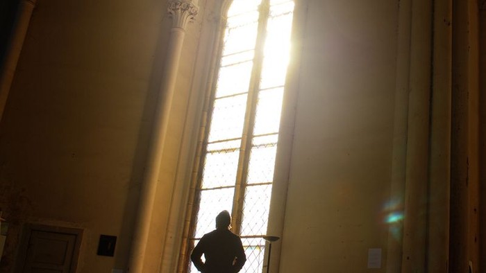 Mann steht vor großem Kirchenfenster im Sonnenlicht