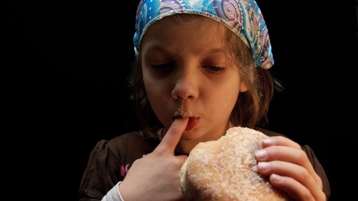 Ein kleines Mädchen mit bunter Mütze genießt ein Donut.