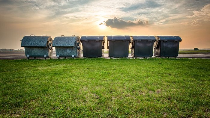 Sechs Mülltonnen stehen in einer Reihe auf einem grasbewachsenen Feld bei Sonnenuntergang