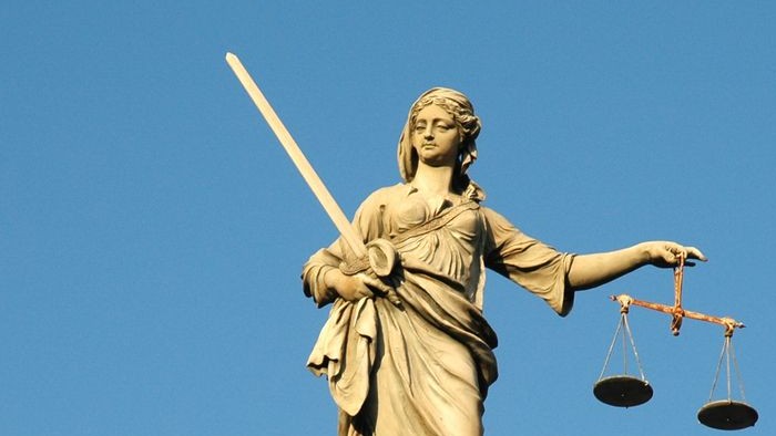 Die Statue einer Frau mit Schwert und Waage vor blauem Himmel