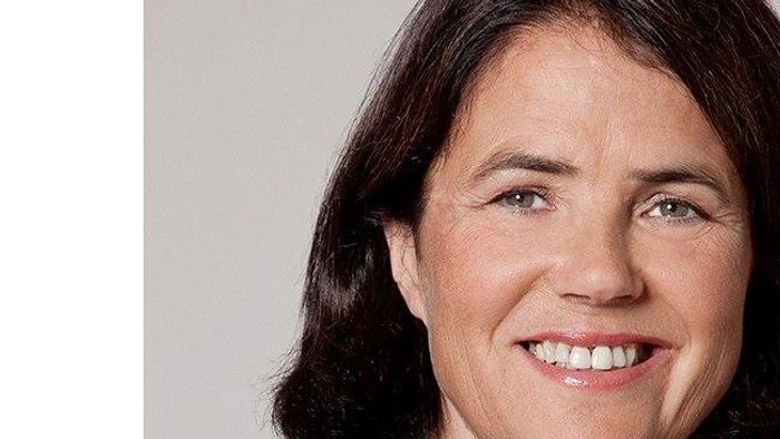 Eine Frau mit dunklem Haar und einem schwarzen Blazer lächelt in die Kamera.