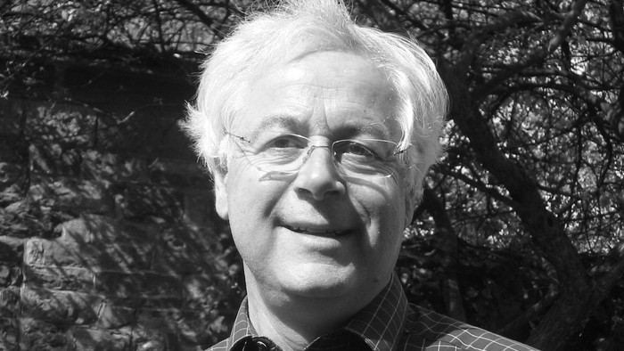 Ein älterer Mann mit Brille und Krawatte lächelt in die Kamera.