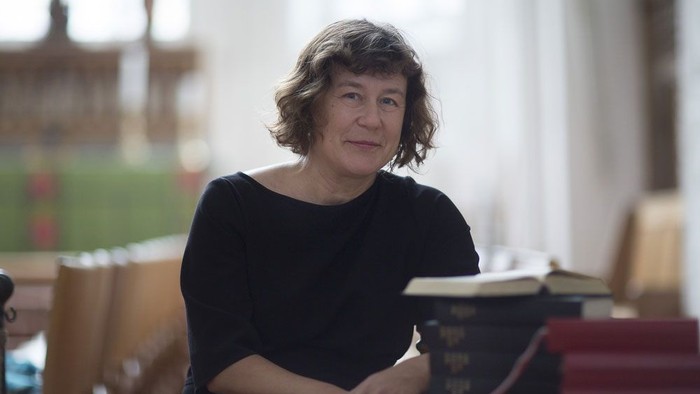 En kvinde sidder i et bibliotek med bøger og skabe i baggrunden.