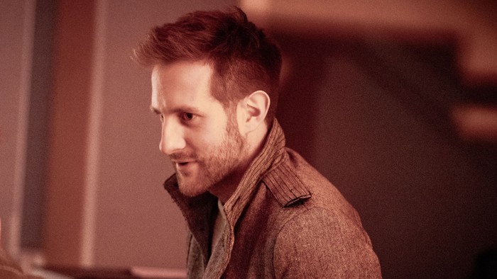 Mann mit Kopfhörer sitzt an einem Tisch und unterhält sich.