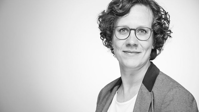 Frau mit Brille und Jacket posiert für ein Schwarz-Weiß-Foto.